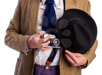 retro paparazzi in a suit and tie secretly takes a photo on a film camera hiding behind a hat