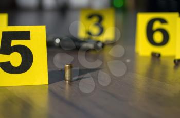 pistol cartridges scattered on the floor next to the crime scene weapons and yellow police markings with numbers near the evidence
