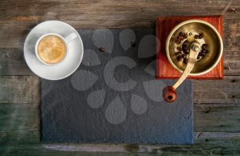 cup of hot aromatic black coffee and an old manual coffee grinder on a background of a dark tray on a wooden table