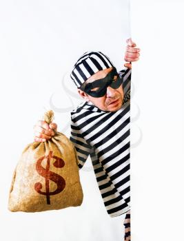 funny operetta gangster in a striped prisoner costume and a black mask with a bag of dollars on a light background
