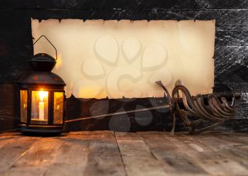 vintage horizontal scroll with place for text on a dark wooden wall, steel sword and lantern with a burning candle