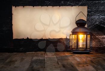 vintage horizontal scroll with place for text on a dark wooden wall and a lantern with a burning candle