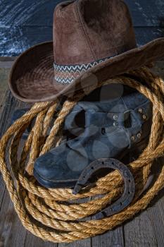 classic cowboy wide-brimmed brown brown lasso hat made of coarse rope and riding boots on a dark wooden background