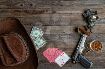 playing cards laid out on an old wooden table in the saloon money, whiskey and a gun for self-defense