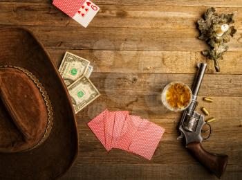 playing cards laid out on an old wooden table in the saloon money, whiskey and a revolver for self-defense