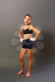little girl in a sports tank top and shorts with hands wrapped in protective bandage is engaged in martial arts on a dark background