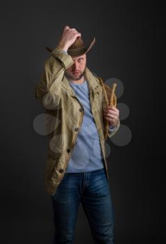 Cowboy in a wide-brimmed hat and jacket with a lasso on his shoulder posing on a dark background