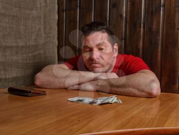 sad man in a rather poor interior looks at the balance of cash in front of him
