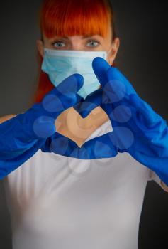 Young girl in a medical mask and rubber protective gloves folded her heart-shaped fingers