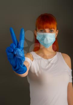Young girl in medical mask and rubber protective gloves shows V victory sign.