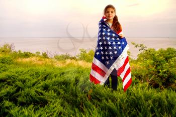 little American girl holding a star striped US flag in her hands on the river bank 