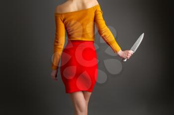 A young girl in a bright skirt and blouse holds in her hands a large steel kitchen knife on a dark background