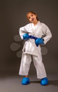 Little girl in a white kimono with a blue belt and equipment rests after a duel on a dark background