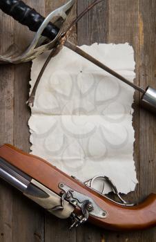 vintage pirate epee and pistol lie on empty parchment on wooden background