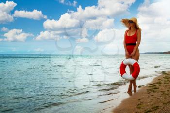 young girl in a closed red retro swimsuit carries a lifebuoy in her hands