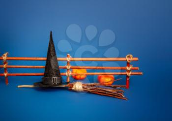 Classic witch black pointed hat and broom for flying near the fence with pumpkins