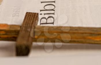 Old with yellowed pages open holy bible and a simple wooden cross close up