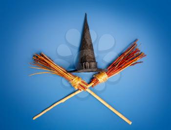 Classic witch black pointed hat and two crossed flying brooms