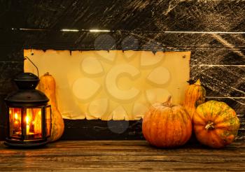 Several assorted small pumpkins on a dark background next to a lighted lantern