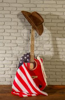 a traditional wide-brimmed cowboy hat, and the Stars and Stripes USA flag hang on a classic acoustic guitar