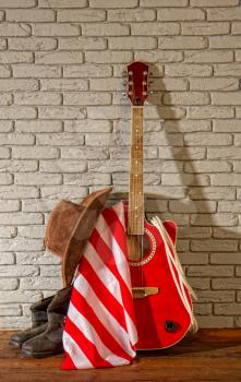 the traditional wide-brimmed cowboy hat, and the stars-striped US flag lie next to a classic acoustic guitar