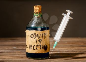 Dirty artisanal bottle with a fake coronavirus vaccine made in unsanitary conditions and a syringe