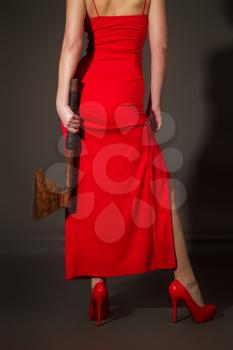 Slender elegant girl in a red evening dress with a huge iron ax in her hands for self-defense on a dark gray background