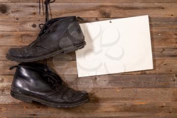old black leather men's shoes on a background of a wooden plank wall next to a sheet of paper with a place for text