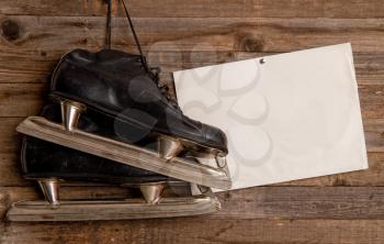 old black ice hockey skates hang against a wooden plank wall background next to a sheet of paper with space for text
