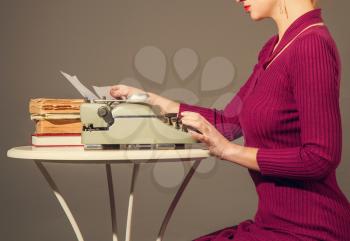 A slender elegant girl in a dress is typing something on an old typewriter