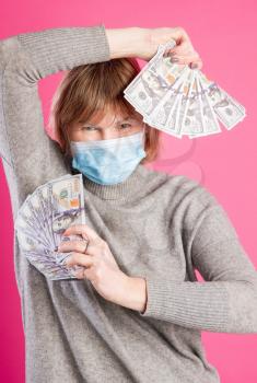 Adult woman in protective medical mask rejoices in sudden wealth or gain against bright pink background