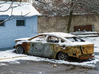 abandoned very burnt car on the street under the snow 