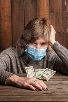 An adult poor woman in a medical protective mask looking sadly recounts her last dollars during a crisis