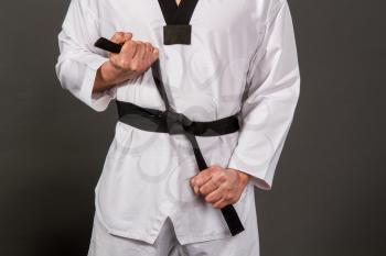 Strong male athlete in white taekwondo kimono puts on sensei black belt