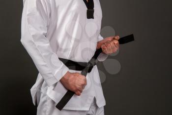 Strong male athlete in white taekwondo kimono puts on sensei black belt