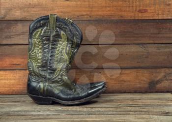 Shabby old ornate classic cowboy boots on wooden background