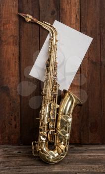 elegant classic musical instrument bronze saxophone on old wooden background with sheet of blank paper with place for text