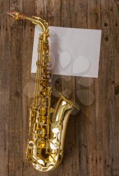 elegant classic musical instrument bronze saxophone on old wooden background with sheet of blank paper with place for text