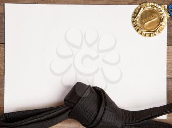 Blank paper for your text with a black karate belt and a gold medal for first place spread out next to it