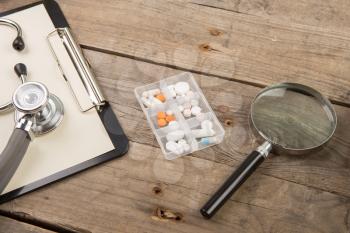 Workplace of a doctor. Stethoscope, clipboard, pills and other stuff on wooden desk