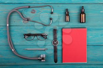Workplace of doctor - stethoscope, medicine clipboard, glasses and watches on wooden desk