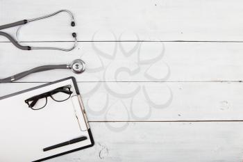 Workplace of doctor - stethoscope, medicine clipboard, glasses  on wooden desk