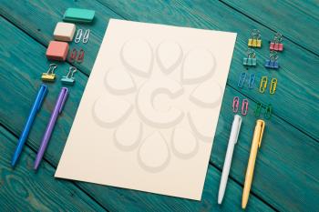 Blank sheet of paper and colorful office accessories on a wooden table 