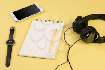 Smartphone, notepad, headphones, pen and watch on the yellow background 