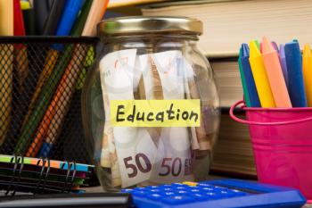 School supplies and glass jar with money for education on wooden table with open books