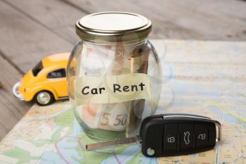 Car rental concept - car key and money jar on the road map