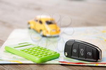 Car rental concept - car key and calculator on the road map