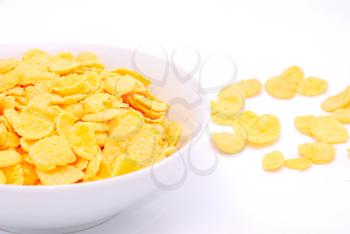 Gold corn flakes heaped in the white dish and on the white table.