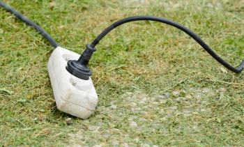 Old white plastic extension adapter plug cable on the ground at garden.