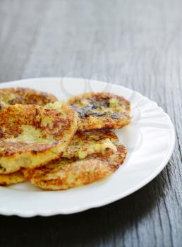 Fresh fried zucchini potato pancakes on a white plate on the wooden table.
